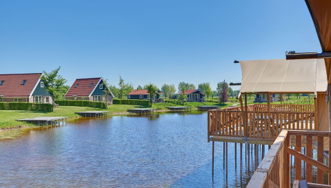 Vue sur les tentes glamping et maisons de vacances au bord d’un lac au Holiday park Eigen Wijze, Pays-Bas, soleil.