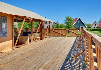 Spacious wooden deck by a safari tent at Holiday park Eigen Wijze, Netherlands, with cabins in view.