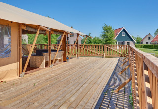 Amplia terraza de madera junto a tienda safari en Holiday park Eigen Wijze, Países Bajos, con cabañas al fondo.