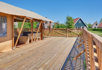 Amplia terraza de madera junto a tienda safari en Holiday park Eigen Wijze, Países Bajos, con cabañas al fondo.