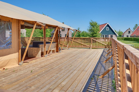 Amplia terraza de madera junto a tienda safari en Holiday park Eigen Wijze, Países Bajos, con cabañas al fondo.