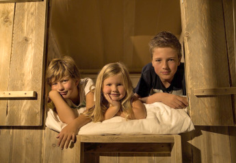 Three smiling children relax together in a cozy safari tent at Holiday park Eigen Wijze in the Netherlands.
