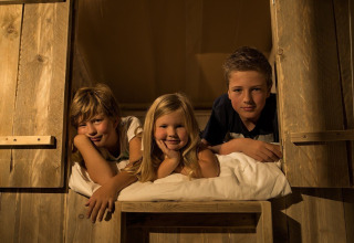 Tres niños sonrientes descansan juntos en una acogedora tienda safari en Holiday park Eigen Wijze, Países Bajos.
