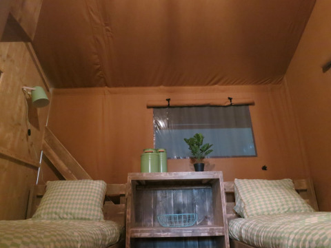 Interior de tienda safari con dos camas individuales, estantería de madera y detalles verdes en Eigen Wijze.