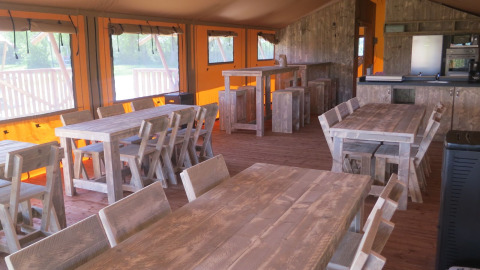 Interior of a group safari tent with rustic wooden tables at Holiday park Eigen Wijze in the Netherlands.