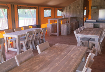 Binnenkant van een groep safaritent met houten tafels bij Holiday park Eigen Wijze, Nederland.