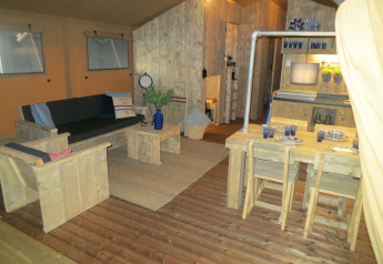 Interior of a safari tent, featuring wooden furniture, lounge, and dining area at Holiday park Eigen Wijze.