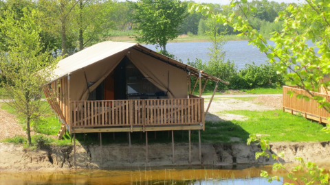 Tienda safari sobre pilotes junto al lago en Holiday park Eigen Wijze, Países Bajos, rodeada de árboles verdes.