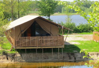 Safari tent on stilts by a lake at Holiday park Eigen Wijze, Netherlands, surrounded by green trees.