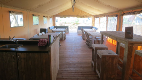 Interior view of spacious safari tent group accommodation with wood floor, tables, and seating areas.