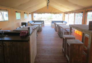 Interior view of spacious safari tent group accommodation with wood floor, tables, and seating areas.