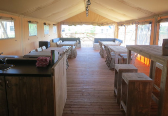 Vue intérieure d’une grande tente safari avec sol en bois, tables et espaces de détente pour groupes.