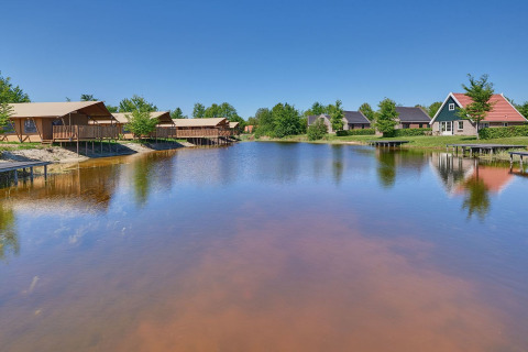 Vue sur un lac paisible avec tentes glamping luxueuses et cottages au Holiday park Eigen Wijze aux Pays-Bas.