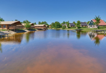 Vue sur un lac paisible avec tentes glamping luxueuses et cottages au Holiday park Eigen Wijze aux Pays-Bas.