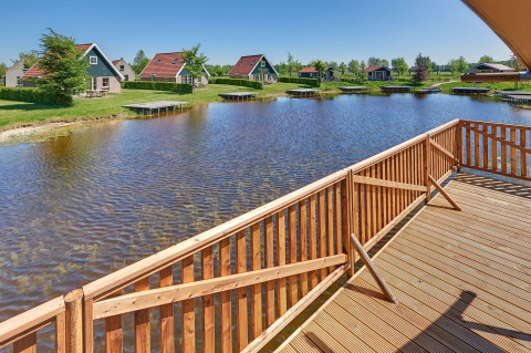 Blick von einer Holzterrasse über einen Teich auf Glamping-Zelte und Hütten im Ferienpark Eigen Wijze.