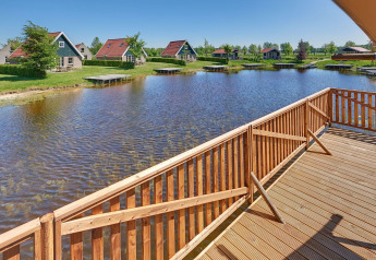 Vista da una terrazza di legno su uno stagno con tende glamping e cottage ad Holiday park Eigen Wijze, Olanda.