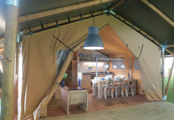 Interior view of a safari tent with dining table, chairs, and kitchen at Holiday park Eigen Wijze, Netherlands.