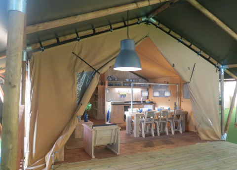 Interior view of a safari tent with dining table, chairs, and kitchen at Holiday park Eigen Wijze, Netherlands.