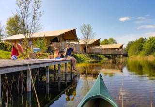 Familia relajándose junto al agua y tiendas safari en Holiday park Eigen Wijze, Países Bajos, con canoa.
