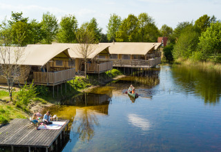 Tiendas safari junto al lago con huéspedes, terrazas de madera y canoa en Holiday park Eigen Wijze, Países Bajos.