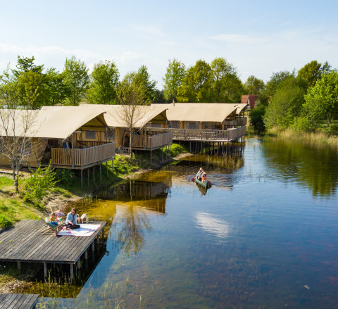 Tiendas safari junto al lago con huéspedes, terrazas de madera y canoa en Holiday park Eigen Wijze, Países Bajos.