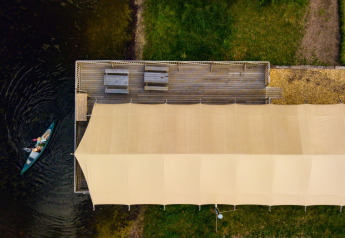 Vista aerea di una tenda safari vicino a un lago, una canoa e panche su una piattaforma in legno.