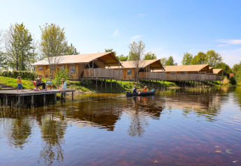 Families relax by the lake and sail canoes near luxury safari tents at Holiday park Eigen Wijze, Netherlands.