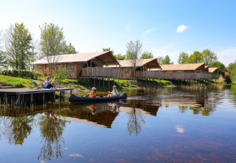 Famiglia in canoa sul lago davanti a tende safari di lusso al Holiday park Eigen Wijze, Paesi Bassi.
