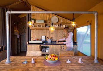 A woman prepares food in a cozy safari tent kitchen with wooden furnishings and warm lighting.