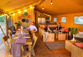 Four people dine and relax inside a luxury safari tent at Holiday park Eigen Wijze in the Netherlands.