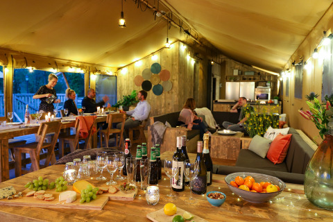 Interior de una tienda de safari glamping de lujo con invitados cenando y relajándose en Holiday park Eigen Wijze.