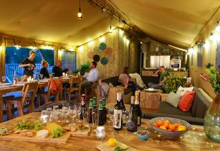 Interior de una tienda de safari glamping de lujo con invitados cenando y relajándose en Holiday park Eigen Wijze.