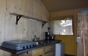 Kitchen area of the Comfort safari tent at Camping 't Veld in the Netherlands, featuring stove and fridge.