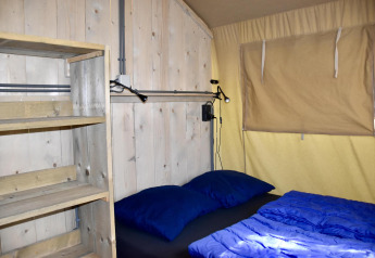 Inde i en Comfort safari-telt på Camping 't Veld, Nederlandene, med en seng, træhylder og vindue.