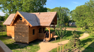 A charming wooden glamping cabin called Heydehuis, surrounded by lush greenery and sunny garden paths.