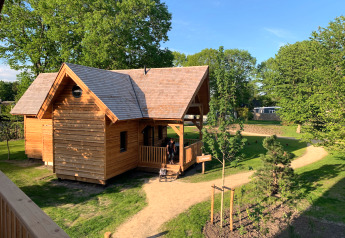 Sfeervolle houten glamping-accommodatie Heydehuis, omringd door groene bomen en zonnige wandelpaden.
