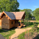 Cabane en bois pour glamping nommée Heydehuis, entourée d’arbres verts et de chemins baignés de soleil.