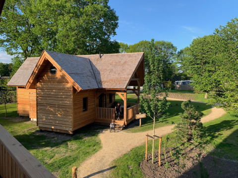 Acogedora cabaña de madera para glamping llamada Heydehuis, rodeada de árboles verdes y senderos soleados.