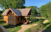 Acogedora cabaña de madera para glamping llamada Heydehuis, rodeada de árboles verdes y senderos soleados.