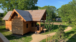 Ein charmantes Glamping-Holzhaus namens Heydehuis, umgeben von grünen Bäumen und sonnigen Wegen.