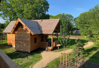 Acogedora cabaña de madera para glamping llamada Heydehuis, rodeada de árboles verdes y senderos soleados.