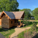 Acogedora cabaña de madera para glamping llamada Heydehuis, rodeada de árboles verdes y senderos soleados.