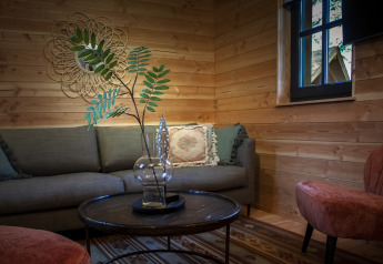 Gezellige Heydehuis glamping woonkamer met houten muren, moderne sofa, glazen vaas en zachte stoelen.