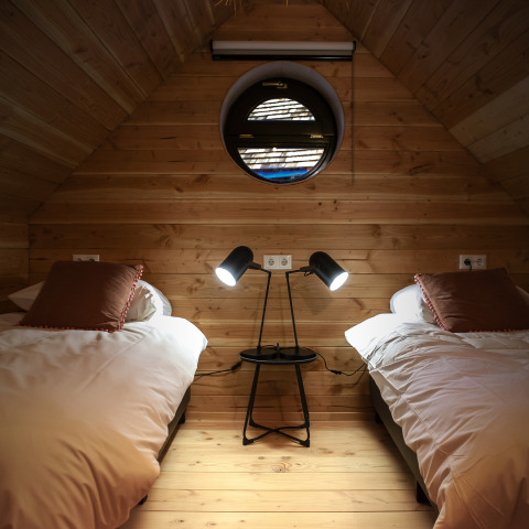 Gemütliches Zimmer im Heydehuis in Sandberghe, Niederlande, mit zwei Betten und rundem Fenster.