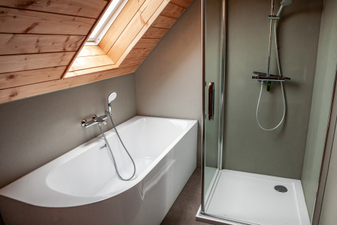 Modern bathroom with a bathtub and shower beneath a wooden slanted ceiling at Heydehuis lodge, Sandberghe.