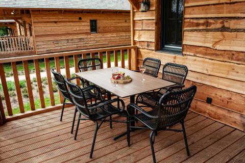 Buiten eethoek op houten veranda bij Heydehuis glamping met zes zwarte stoelen en een tafel.