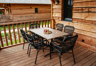 Buiten eethoek op houten veranda bij Heydehuis glamping met zes zwarte stoelen en een tafel.