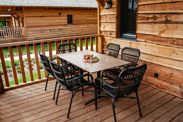 Zona de comedor exterior en un porche de madera en Heydehuis glamping con seis sillas negras y mesa.