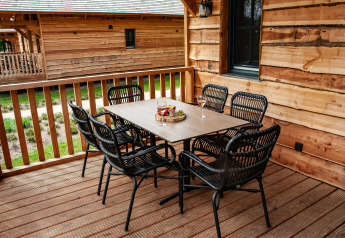 Zona de comedor exterior en un porche de madera en Heydehuis glamping con seis sillas negras y mesa.