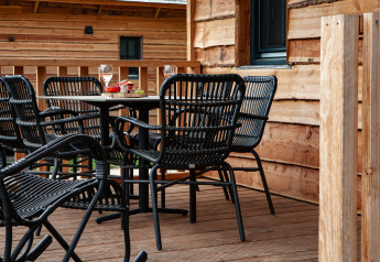 Terraza al aire libre con sillas negras y mesa en Heydehuis glamping, rodeada de paredes de madera.